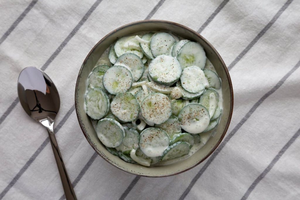 Easy To Make, Easy To Love A bowl of sliced cucumbers mixed with creamy dressing and sprinkled with pepper sits on a cloth with gray stripes. A spoon is placed next to the bowl. MyFitnessPal Blog