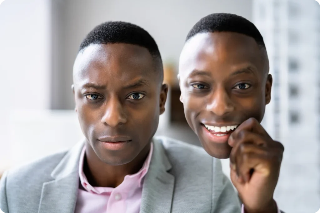 A professional holds a smiling mask beside his unsmiling face, illustrating imposter syndrome.